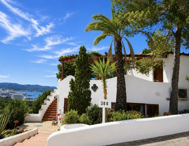 Whitewashed Mediterranean villa on a hillside with palms and a distant sea view